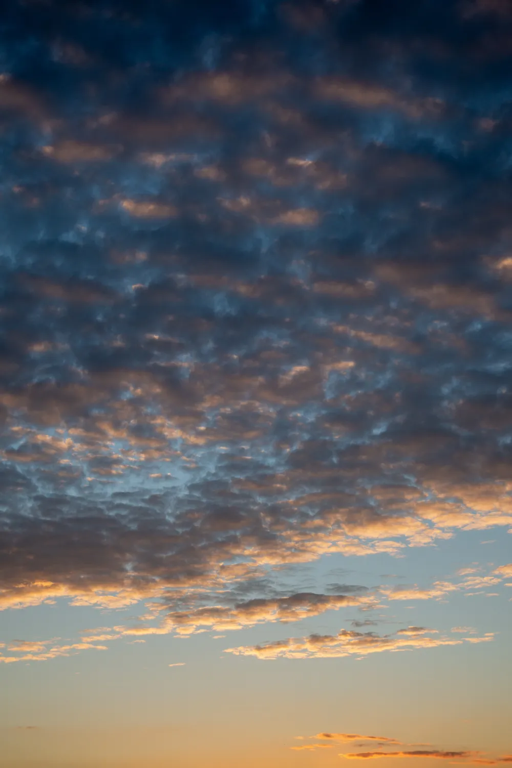 Two cloud covers in the sky during sunset, the nearest one grey, through it the second one lit orange