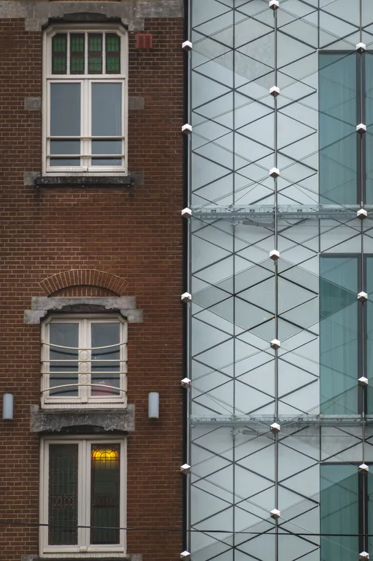 Two buildings side by side, on the left is a traditional Dutch brown brick building, on the right a modern building, white with abstract hexagonal patterns and glass