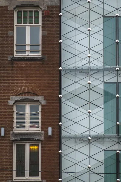 Two buildings side by side, on the left is a traditional Dutch brown brick building, on the right a modern building, white with abstract hexagonal patterns and glass