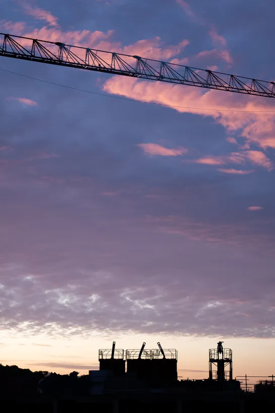 Sunrise, a pink cloud streaks across the sky. A horizontal jib comes right in front of it. Construction can be seen in the shadows below.