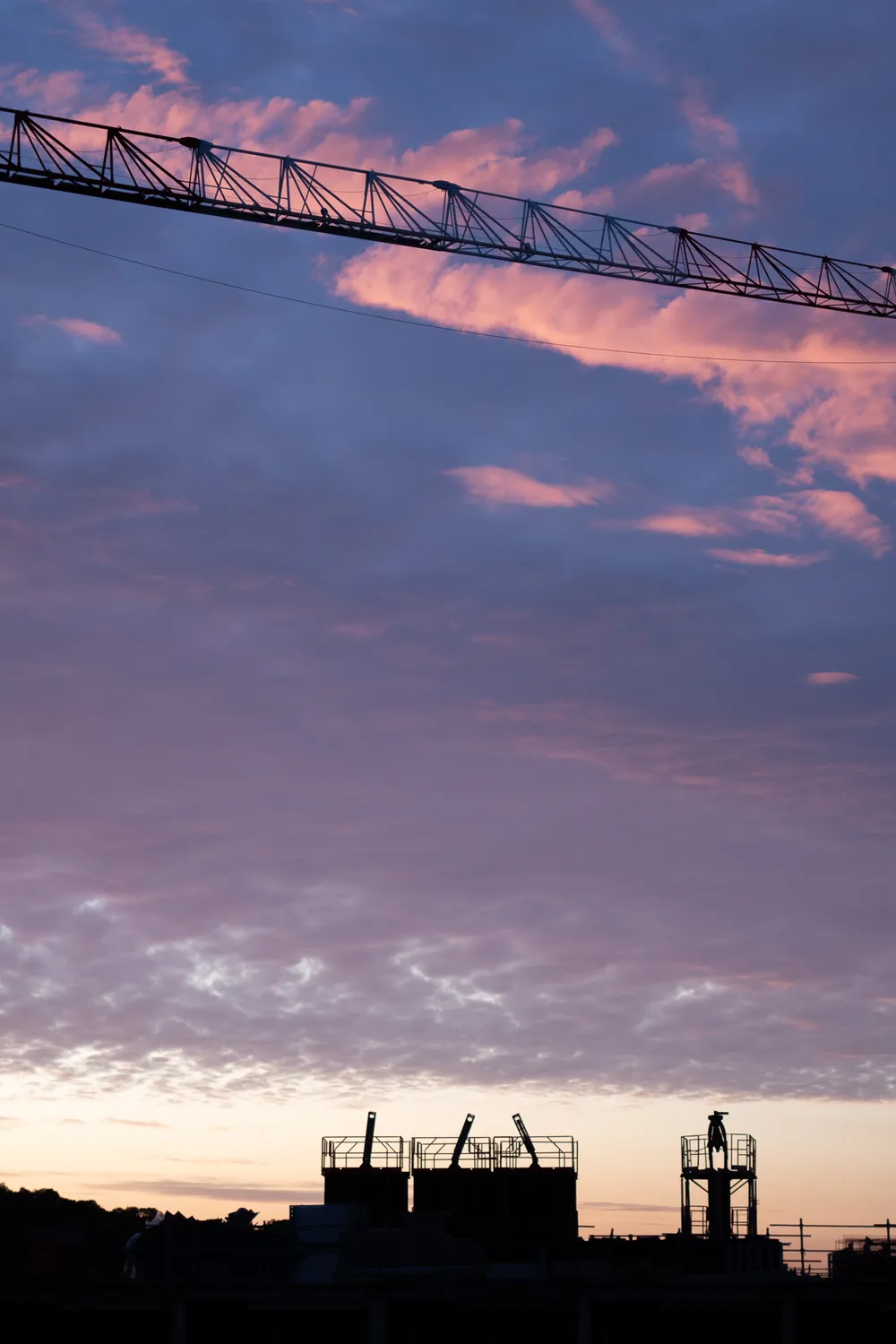 Sunrise, a pink cloud streaks across the sky. A horizontal jib comes right in front of it. Construction can be seen in the shadows below.