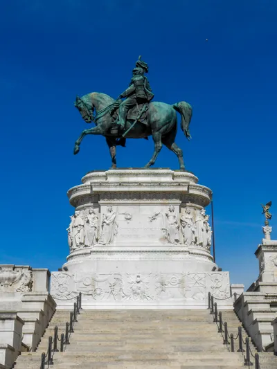 Bronze statue of Vittorio Emanuele on a stone base up some stairs, a blue sky behind