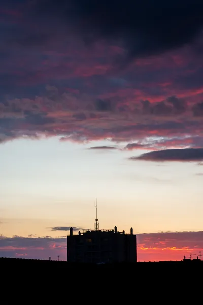 Sunset, partly red clouds above, a dark building at the bottom center