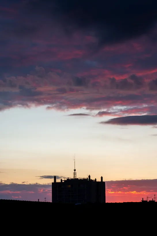 Sunset, partly red clouds above, a dark building at the bottom center