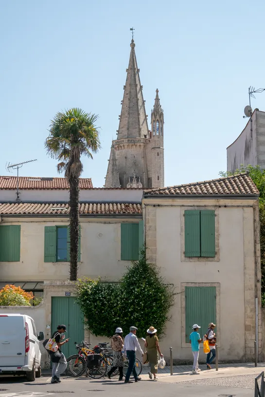 Tourists walking down a street, in front of a building with a palm tree. Behind it all, a tall stone tower