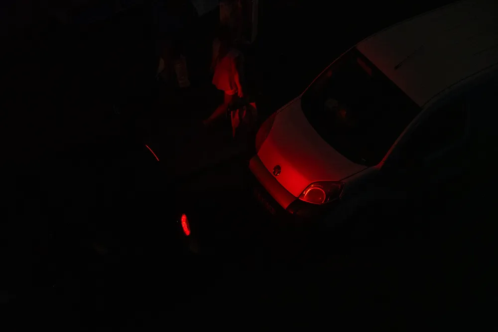 A car's red lights illuminates the car behind and passerbys