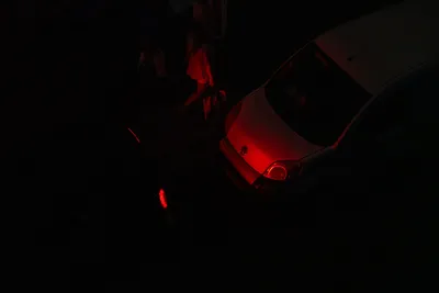 A car's red lights illuminates the car behind and passerbys