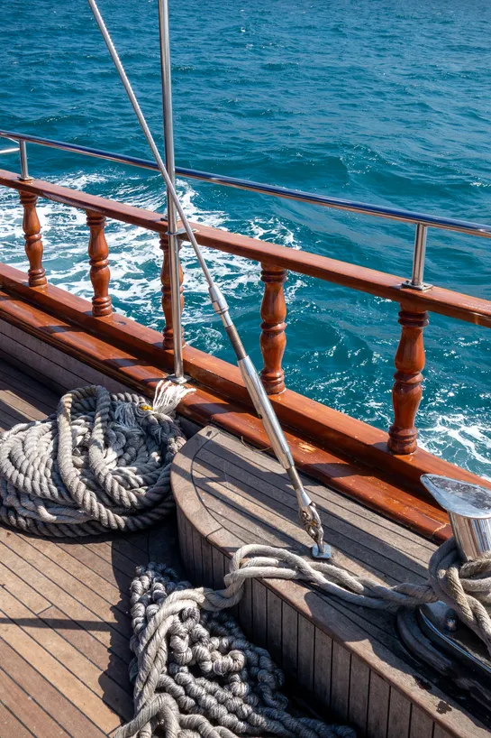 Ropes aboard a boat. Wooden railing and the sea behind.