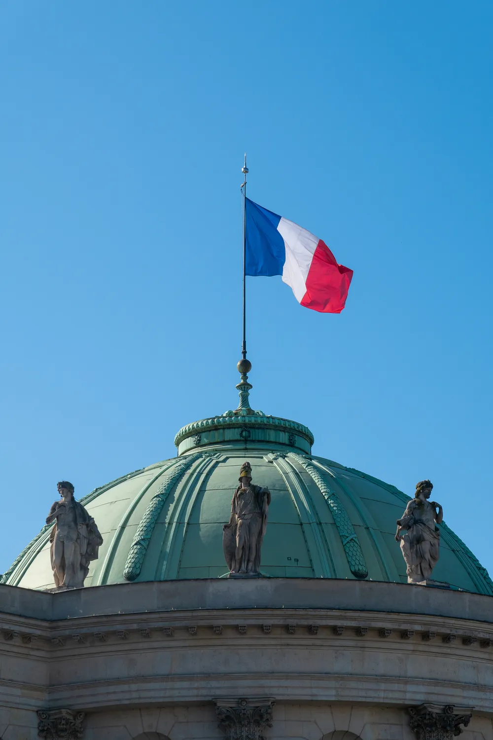 The French flag floats above the dome of the Great Chancellery of the Order of the Legion of Honor, three classical statues visible on the ledge