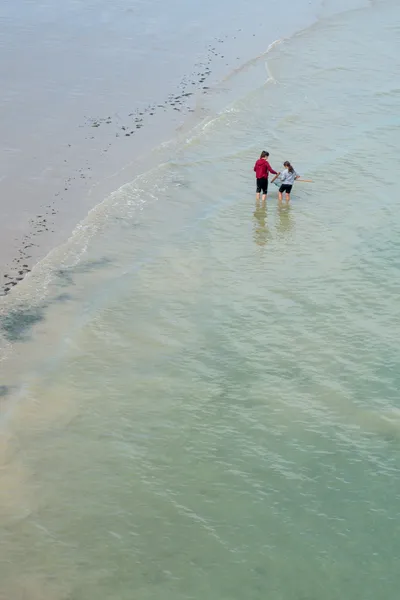 On the beach, in the water, two young people use nets to catch fish
