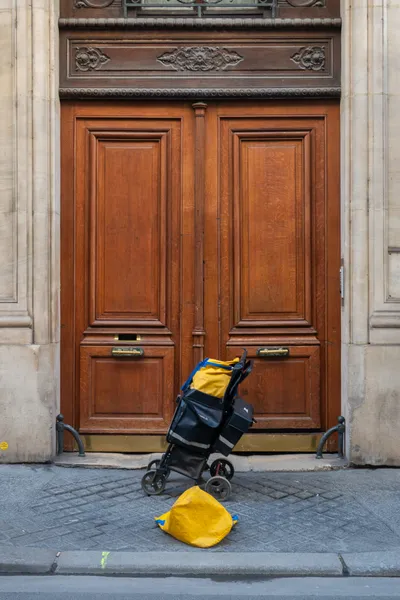 In front of a big Parisian wooden door, a postman has left his bags unattended