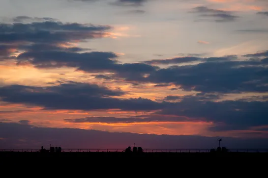 A sunset, with the sun below the horizon but its red glow is still visible. Clouds lit by the sun in the background, a rooftop with chimneys in the foreground.