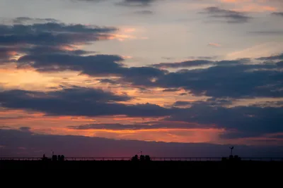 A sunset, with the sun below the horizon but its red glow is still visible. Clouds lit by the sun in the background, a rooftop with chimneys in the foreground.