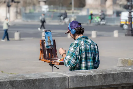 A man with headphones painting a nearby golden statue on a small canvas