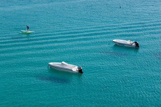 One person paddling near two anchored motorboats, in turquoise waters.