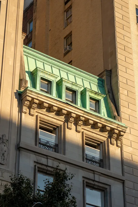 A stone building, with copper roofing, stuck between two much taller buildings.