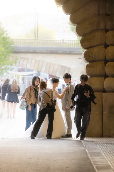 A smiling newlywed couple is being prepped for a photoshoot by a crew