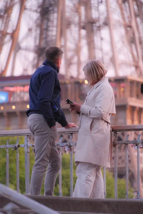 A couple stands on a bridge, the Eiffel Tower structure behind