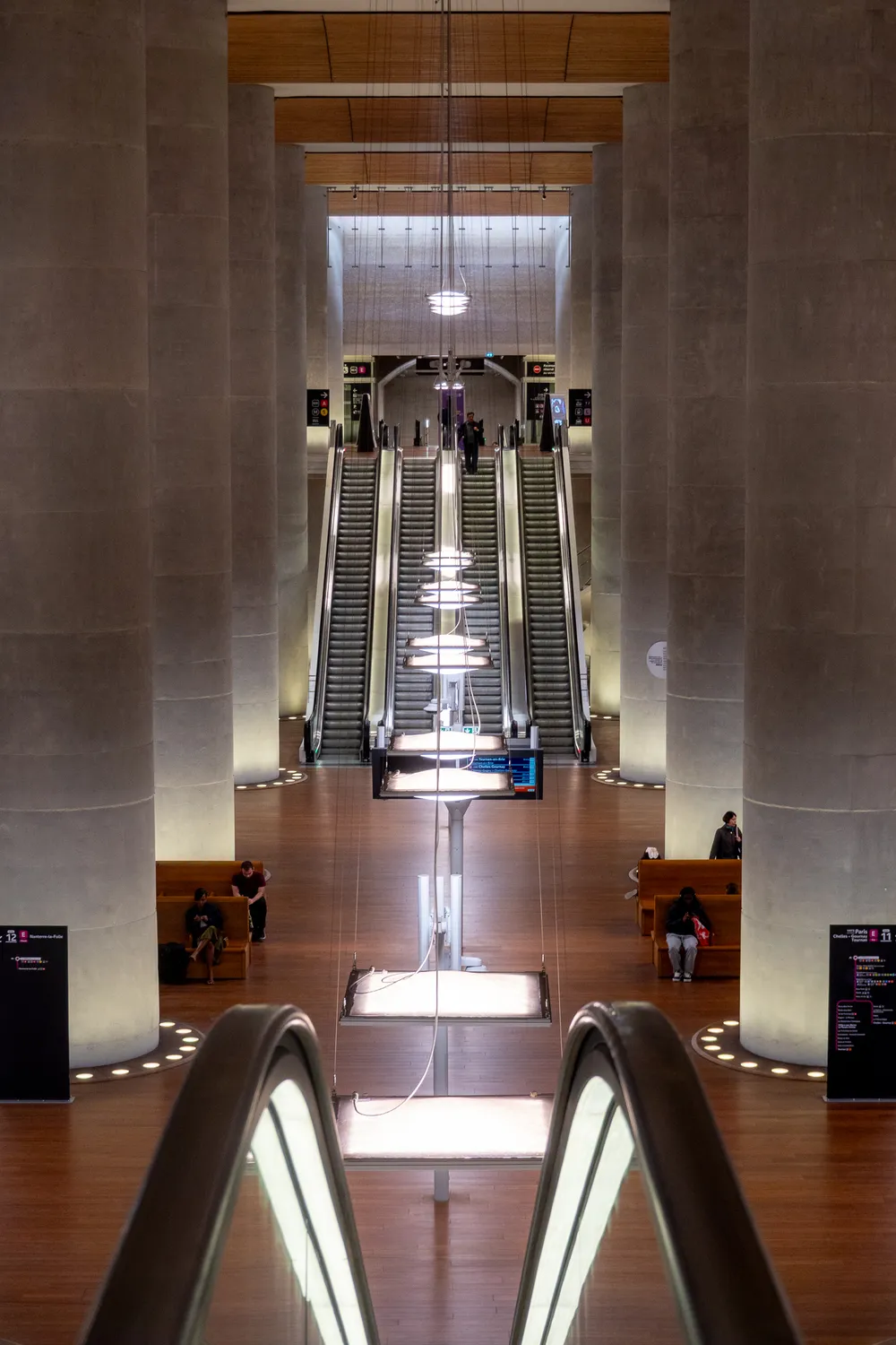 Massive stone pillars and wooden detail surround people in this underground commuter train station