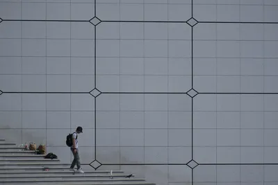 A passerby goes down steps sullied by detritus in front of a grey wall