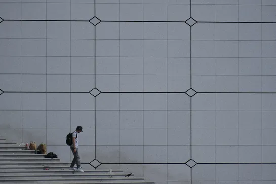 A passerby goes down steps sullied by detritus in front of a grey wall
