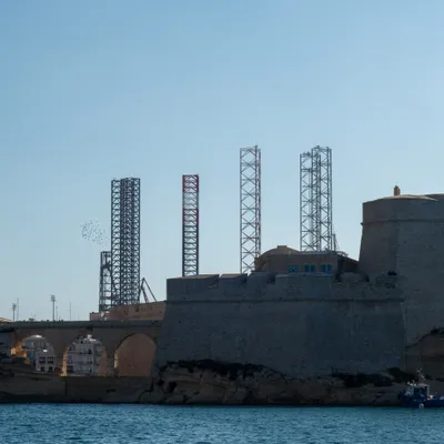Tall metal towers behind stone walls, a large flock of birds flying around