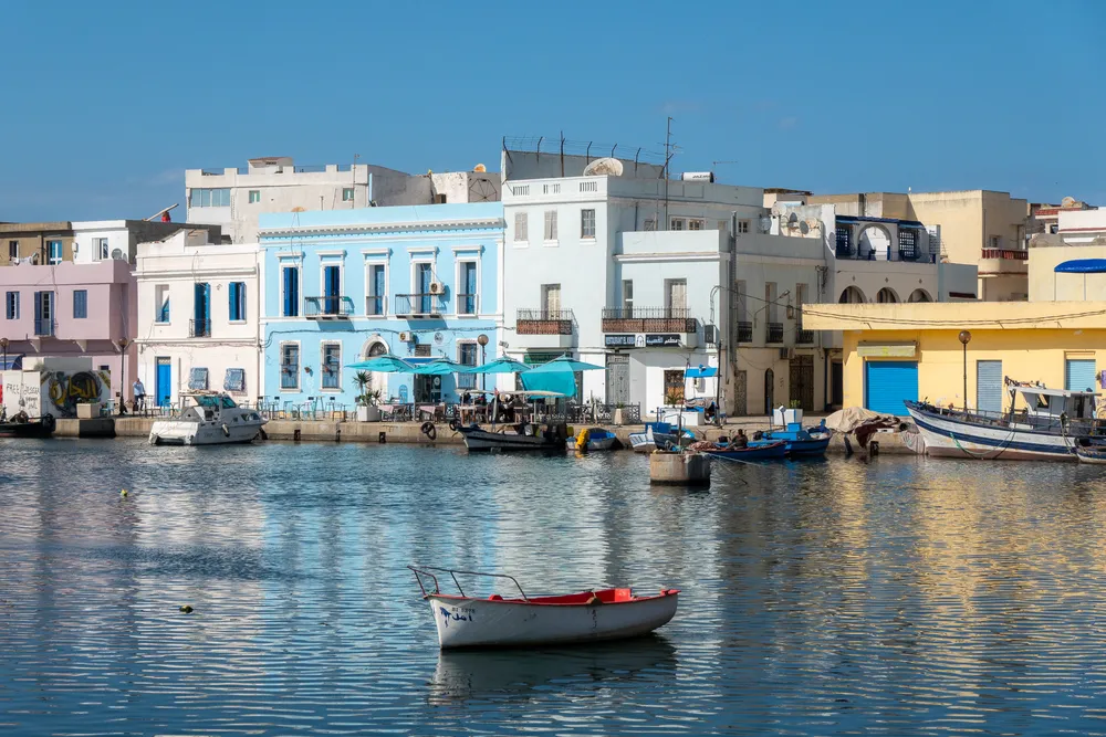 A boat drifts in the old port of Bizerte, pastel buildings in the background