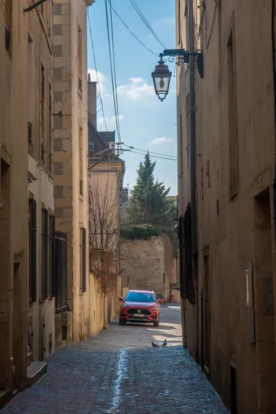 A narrow paved street, one lone red car on the other side