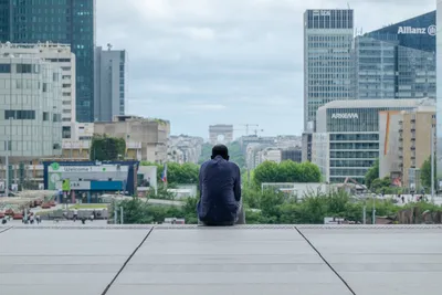 A man sat on steps overlooking La Défense's esplanade and skyscrapers and, in the distance, the Arc de Triomphe