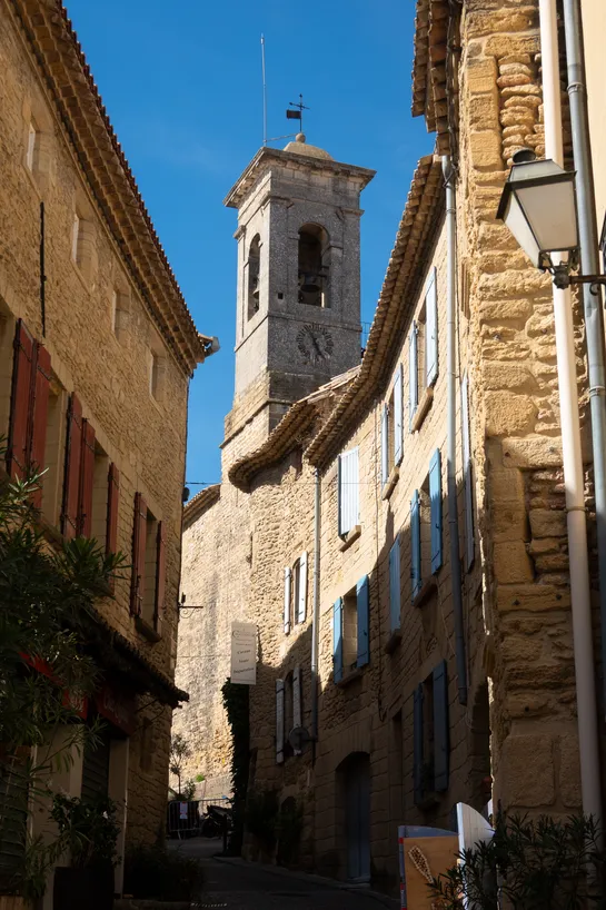 An older, brick church tower standing in the middle of a street with equally old residential buildings