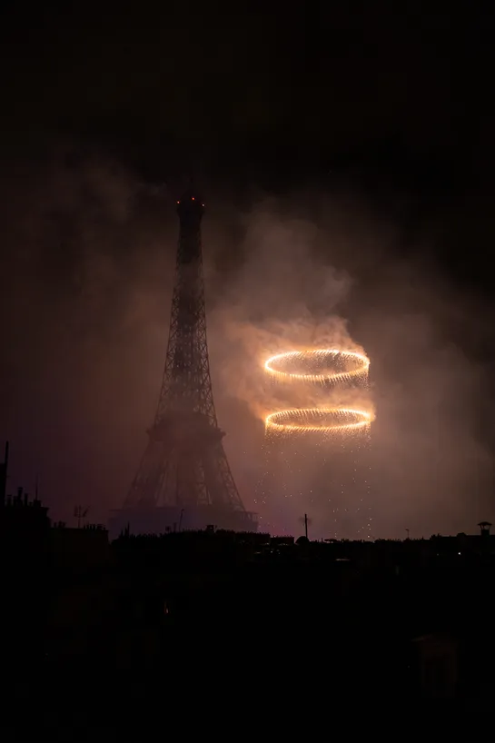 Two very bright circles floating in the sky among a large amount of smoke next to a dark Eiffel Tower