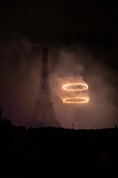 Two very bright circles floating in the sky among a large amount of smoke next to a dark Eiffel Tower