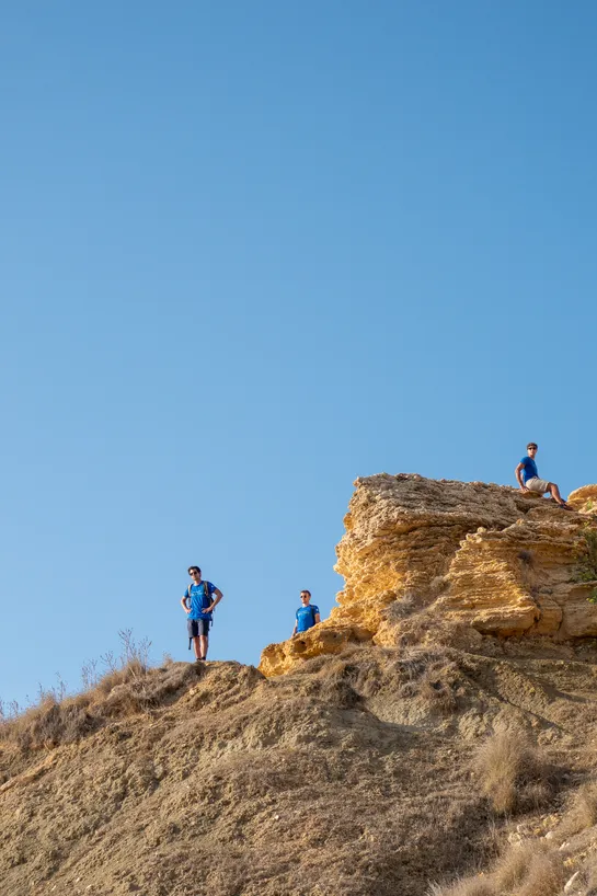 Three tourists, all wearing blue, waiting on top of a cliff