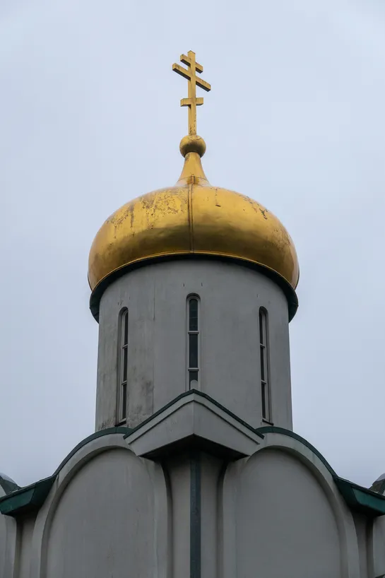 The tower of an orthodox church, its symbol and dome gilded above the otherwise white and plain building