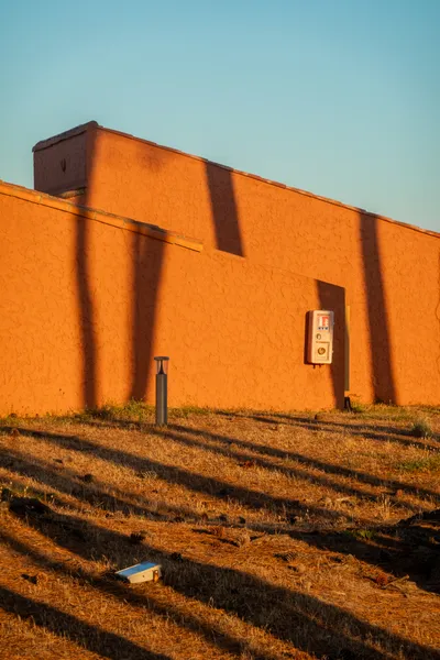 The orange light and tree trunks shadows on the walls of houses