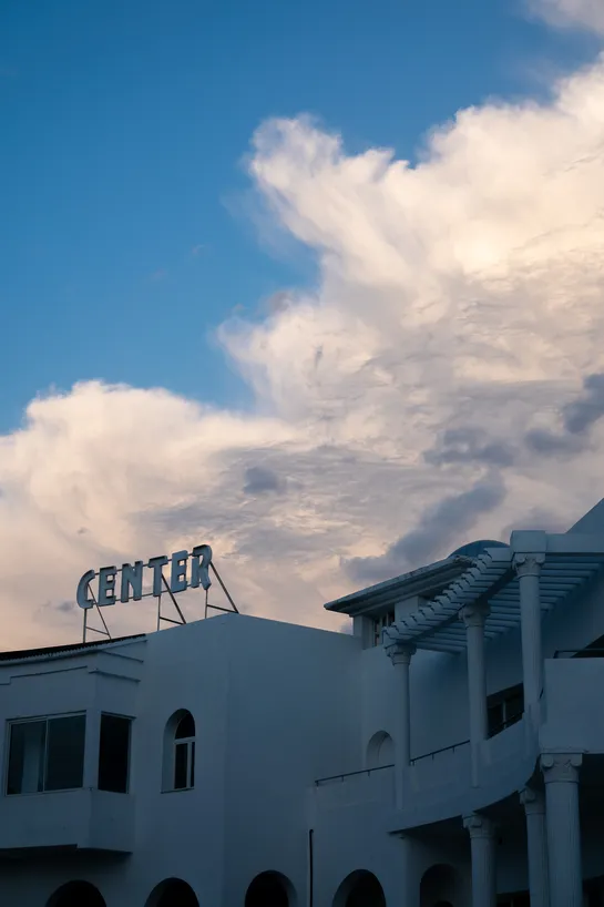 Atop a dim white building, a sign spelling "CENTER", beneath a dramatic sky with cloud strands