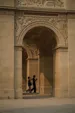 Beneath a very elaborately sculpted stone arch, a couple walks by