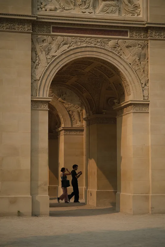 Beneath a very elaborately sculpted stone arch, a couple walks by